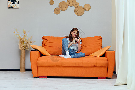 一个长头发女人的肖像 坐在沙发上 电话没有变换过长椅成人橙子快乐女孩微笑公寓互联网房子手机图片