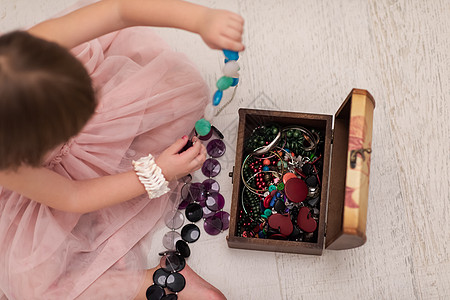 小女孩玩母亲的首饰时享受着快乐蕾丝戏服珠宝盒子手镯头发裙子乐趣珠子地面图片