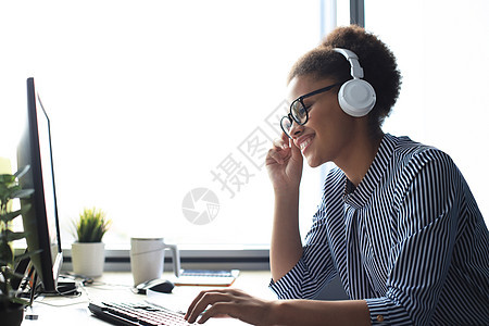 美丽的非洲年轻女性的肖像 在电脑和聊天上工作 坐在耳机里听电话图片