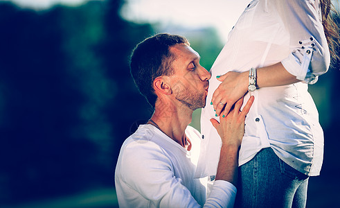 快乐的丈夫拥抱他的怀孕妻子 在公园散步时在公园里母性生活腹部父母微笑幸福父亲男性孩子女士图片