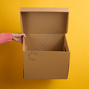 女性手握着黄色背景的棕色露天纸板盒 送货图片