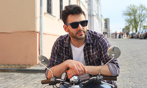 在街上骑一辆老式摩托车的年轻时尚男子帽子男性城市骑术车辆街道阳光发动机摩托旅行图片