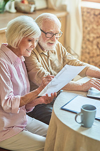 老年男性微笑的老年妇女与其配偶一起检查帐单;背景