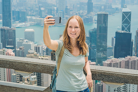 香港太平山女人用智能手机拍自拍杆照片 欣赏维多利亚港的景色 香港凌霄阁顶部的观景台 散焦背景 旅游亚洲概念享受相机成年人游客电话图片