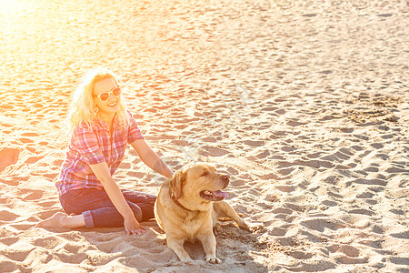 沙滩狗身着太阳镜的年轻美人肖像 坐在沙滩上 带着金色猎犬 海路女孩与狗同行乐趣动物感情运动女孩女性海洋友谊游戏朋友背景