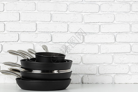 针对白砖墙的一套烹饪锅油炸工作室摄影厨具金属黑色厨房用具白色图片