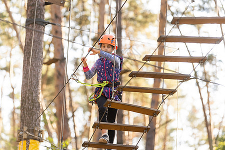 冒险乐园中的女孩攀爬是一个可以包含多种元素的地方 例如绳索攀爬练习 障碍训练场和高空滑索操场头盔公园课程行动风险运动娱乐童年力量图片