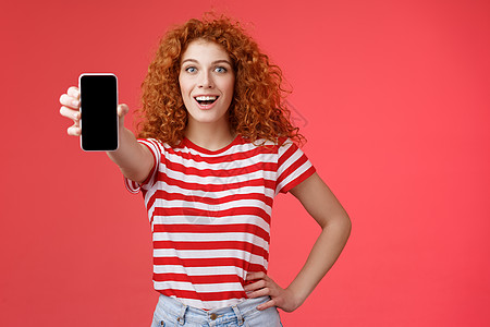 欢快迷人的魅力欧洲红发女孩卷发秀智能手机屏幕快乐地微笑推广应用程序建议推荐良好的应用程序社交媒体页面红色背景女朋友压痛广告展示消图片