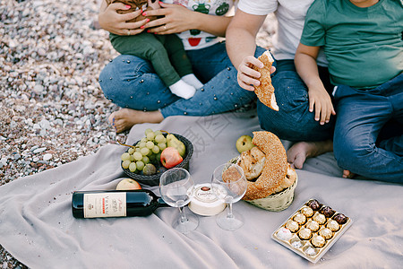 男人和女人有孩子在沙滩上 坐在毯子上吃着食物图片