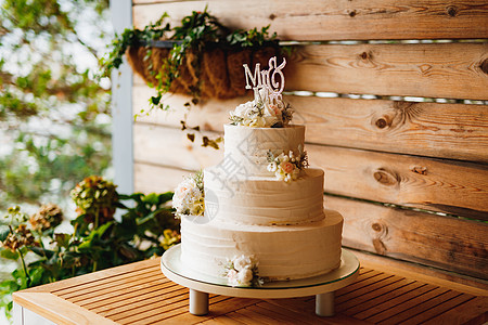 白色的三层结婚蛋糕 在木桌上放鲜花图片