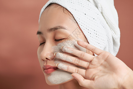 美丽快乐的亚洲少女 运用面部粘土面具 美容治疗 在光线背景上隔离打扫清洁护理黏土刷子女性去角质滋润乐趣皮肤图片