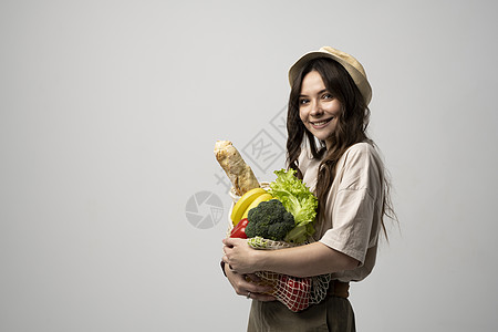 快乐微笑的年轻女子的画像 穿着米色超大号 T 恤 在白色背景下拿着可重复使用的网袋和杂货 可持续性 生态生活和人们的观念图片