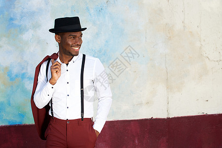 年轻快乐的黑人男子 带着吊带和帽子在墙边微笑图片