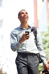 快乐的青年男子在城市中用手机和手提袋行走图片