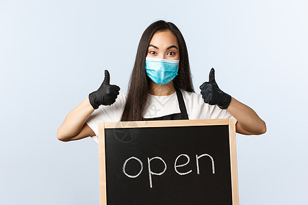 小型企业 covid-19 流行病 预防病毒和员工概念 戴着医用面具的乐观的亚洲女店员 咖啡馆员工或咖啡师竖起大拇指 我们是开放图片