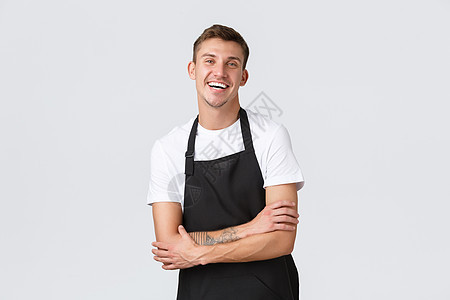 小企业主 咖啡店和员工的概念 热情的微笑 穿着黑色围裙的英俊侍者 开心地笑着 为客户服务 在咖啡馆工作 站在白色背景图片