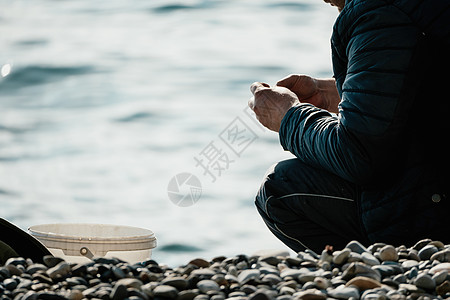 清凉海边海上钓鱼的人爱好收紧鱼线卷轴 平静的海面 渔夫的特写镜头用手在鱼竿上扭动渔线轮 在户外的蓝色大海中钓鱼纺纱运动消遣男性铸件天空行背景