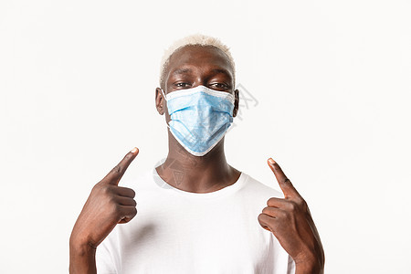 非洲裔美国金发帅哥的特写 手指指着医用面具 在冠状病毒大流行期间穿着防护装备 白色背景背景图片