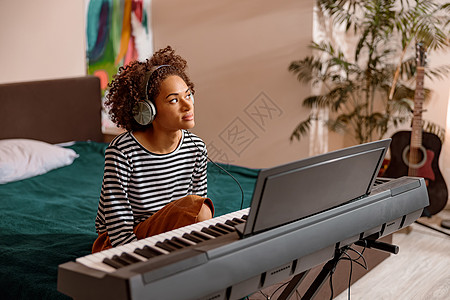 多种族妇女坐在家中靠近合成器的多种族妇女音乐键盘耳机律师词曲卧室音乐家演员闲暇电子图片