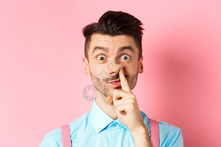 滑稽的白人男子挖鼻子的特写镜头 傻傻地盯着镜头 站在粉红色背景中胡子商业男人发型广告快乐微笑吊带裤成人领结图片