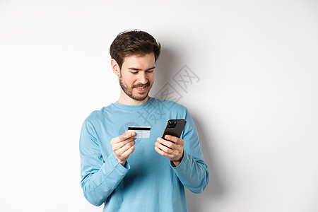 电子商务和购物概念 微笑的男人在线订购 将信用卡号码复制到手机应用程序 站在白色背景上电话银行快乐情绪金融工作室办公室促销成人胡图片