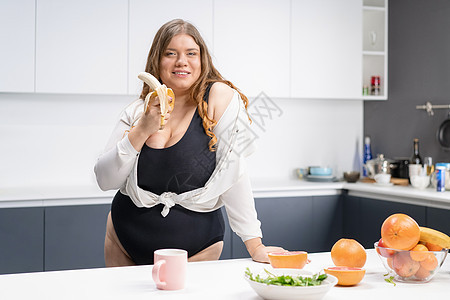 饮食和营养概念 快乐的卷曲身体年轻女子 长金发长发 在现代厨房使用搅拌机 将新鲜果子混合起来用于健康溜冰脂肪肥胖食物尺寸午餐女孩图片