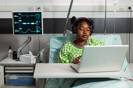 躺在床上看笔记本电脑上网上喜剧漫画的非裔美国人病病人图片