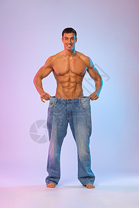 年轻人展示他穿着大牛仔裤瘦了多少体重 胖得难以理解 健康海报饮食肌肉身体重量手术男性营养暴饮暴食男人微笑背景图片