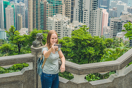 香港太平山女人用智能手机拍自拍杆照片 欣赏维多利亚港的景色 香港凌霄阁顶部的观景台 散焦背景 旅游亚洲概念相机顶峰观光游客成年人图片