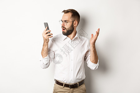 男人在谈话后对手机看不清 站在白背景上迷惑不解的一面雇主工作室商务技术购物困惑经纪人广告工作成功图片