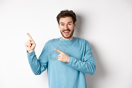 穿着休闲蓝色运动衫的快乐白人男子 手指指着左上角 在白色背景上显示链接或标志 对着镜头微笑商业促销发型成人生活办公室胡子男人示范背景图片