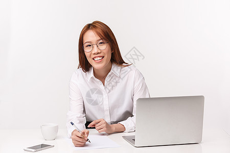 职业 工作和女企业家的概念 特写肖像友善礼貌的亚洲女性 办公室经理与客户签署协议 写下信息 坐在笔记本电脑旁 微笑的相机图片
