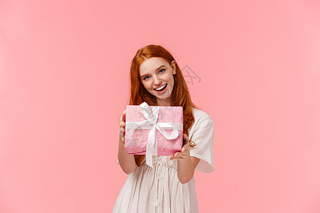 给你 可爱温柔 女性化的红发女孩给你她的礼物 拿着包裹的盒子 祝贺生日 情人节快乐 微笑 站着粉色背景图片