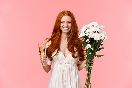 迷人而兴奋的浪漫红发女友收到礼物 拿着白色花束和玻璃香槟 喝酒庆祝 有完美的情人节约会 粉红色背景图片