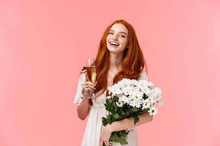 迷人 开朗的 b-day 女孩 一头红色卷发 在聚会 生日庆祝活动中与朋友交谈时 笑着 无忧无虑地看着镜头 拿着花束白花和香槟杯图片
