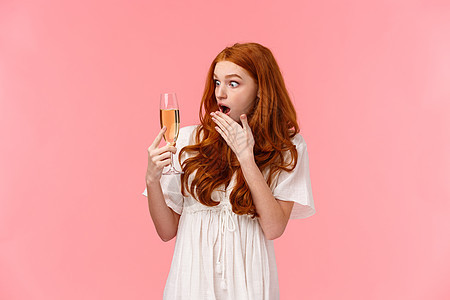 震惊和震惊的红头发女人惊讶地想不起她什么时候喝过香槟酒 有饮酒问题 意识到在聚会上喝得太多 站在粉红色的背景下图片