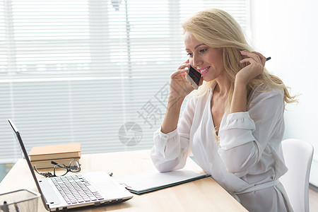 商业 技术和通信概念  金发女郎一边看笔记本电脑一边打电话女性学生操作办公室女士互联网眼镜桌子蓝色经理图片