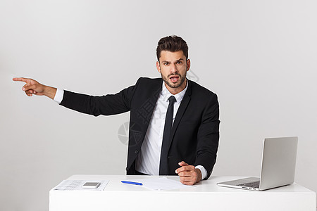 愤怒的商务人士坐在桌子上 尖叫在灰色背景上 看镜头时商业扶手职业男人成人电脑男性办公室经理套装图片