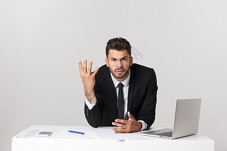 愤怒的商务人士坐在桌子上 尖叫在灰色背景上 看镜头时男性经理技术领带电脑老板套装扶手压力职业图片