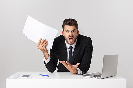愤怒的商务人士坐在桌子上 尖叫在灰色背景上 看镜头时职业办公室男人扶手老板领带男性电脑笔记本压力图片