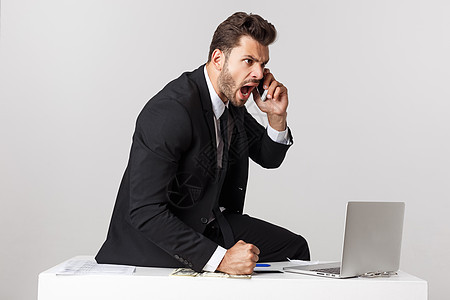 愤怒的商务人士坐在桌子上 尖叫在灰色背景上 看镜头时经理职业男人老板套装领带电脑办公室技术压力图片