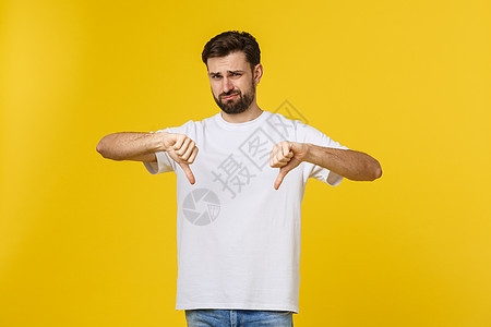 年轻英俊的男人穿着白色 T 恤 在孤立的背景下做着大拇指向下 不同意和同意的表达 疯狂的冲突拇指工作室商业胡须分歧手势协议成人手图片
