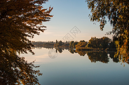 夕阳映衬着收获季节的九月河 树木在水中的倒影 美丽的秋天风景 秋天的颜色倒映在平静的水面上场景蓝色公园城市天空世界太阳地平线游泳图片