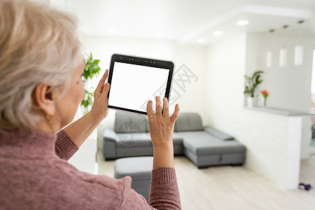 在家的年长妇女站在厨房的厨房里 拿着数字平板电脑控制智能家庭系统后视镜检查摄像头近身图片