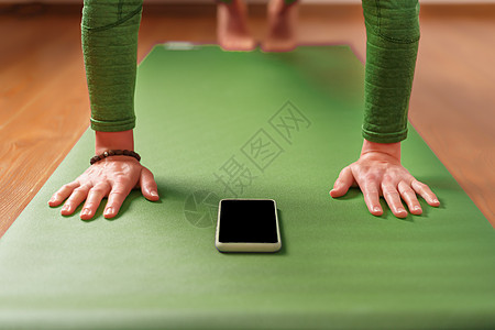 一名妇女坐在绿色运动垫子上时 用智能手机看瑜伽课电话家居生活方式女性训练瓶子运动装女孩公寓锻炼图片