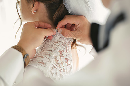 女性用漂亮的发型把婚纱扣在新娘的手上 笑声婚礼手指丝绸衣服奢华蕾丝女孩胸衣幸福房间图片