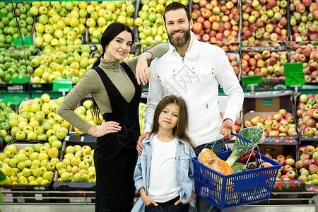 在蔬菜部的超市里 一个快乐的家庭站在一辆满满的手推车上 柜台的背景是苹果成人高清图片素材