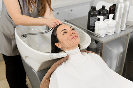 理发师在现代美容院理发前洗了一个年轻的黑发女孩的头发图片