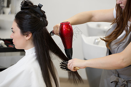 发型师在沙龙里做女人发型工作 用吹风机和圆梳子干棕色长头发图片