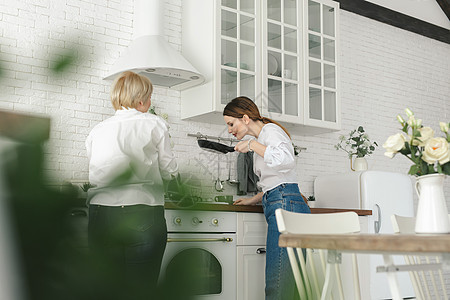 年长的母亲在厨房准备食物 女儿喝茶 看她母亲的眼神图片